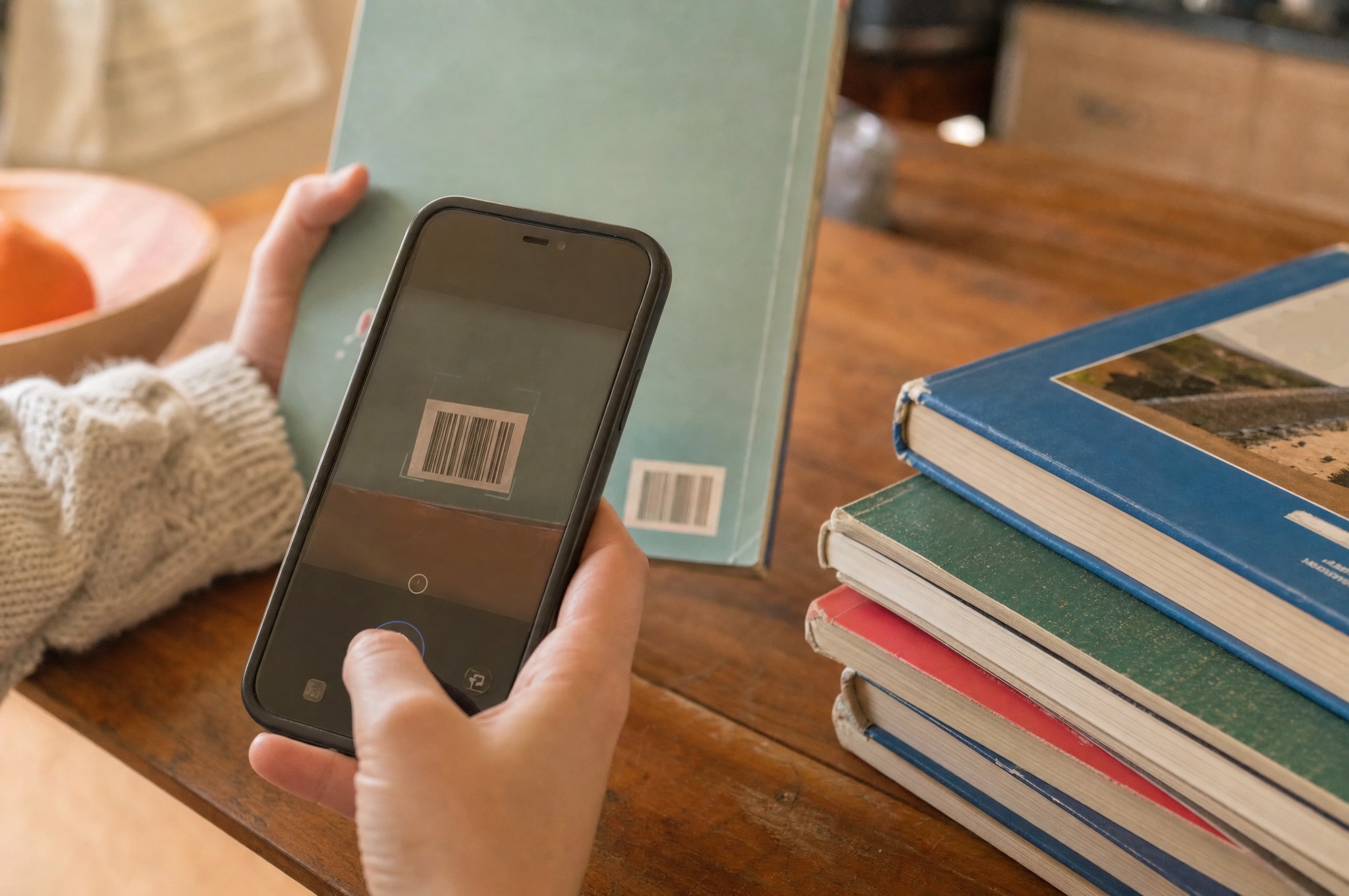 Una mano inquadra con il telefono il codice a barre sul retro di un libro di scuola, su un tavolo di cucina